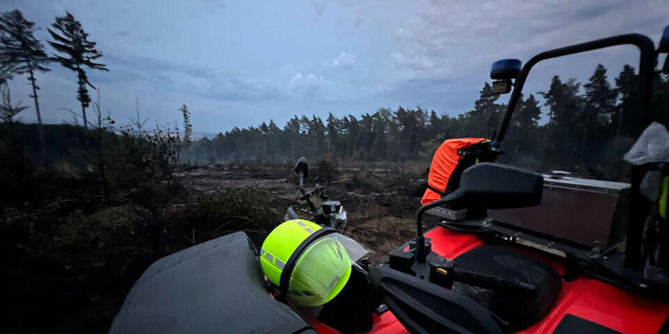 Ein signalgelber Helm liegt auf einem Quad der Johanniter. Im Hintergrund sieht man verbrannte Erde.