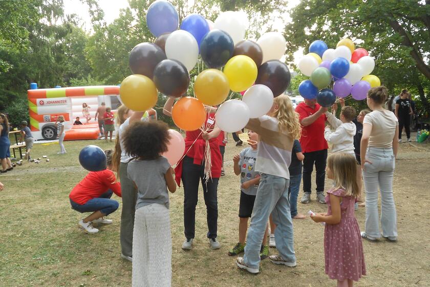 Helfer verteilen Luftballons an die Kinder und Jugendlichen auf einer Wiese.
