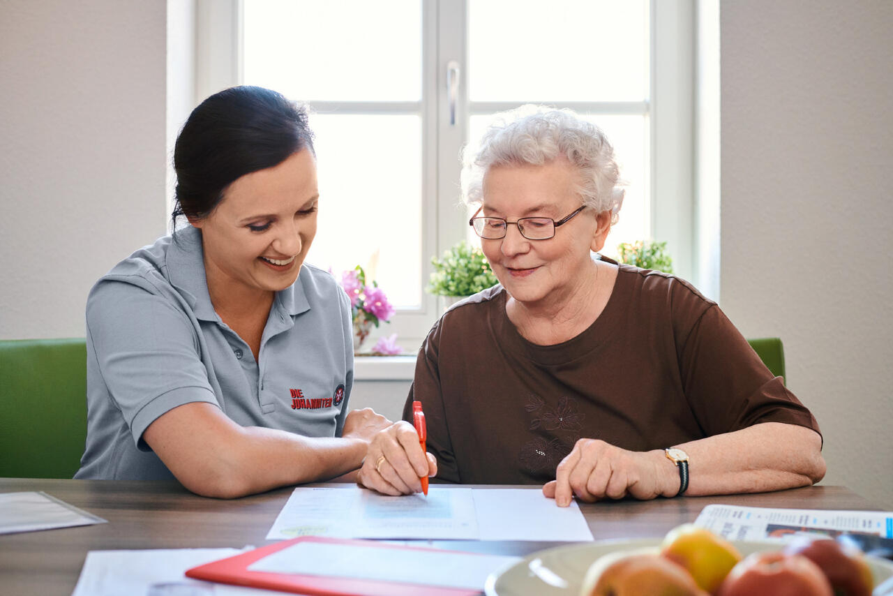 Eine Mitarbeiterin der Johanniter hilft einer älteren Frau beim Ausfüllen von Formularen.