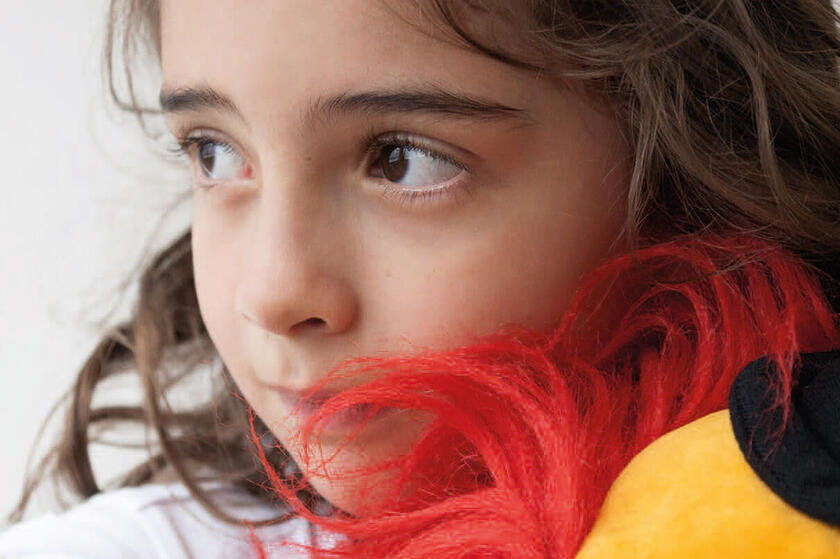 Ein trauriges Mädchen hält einen Plüschclown im Arm.