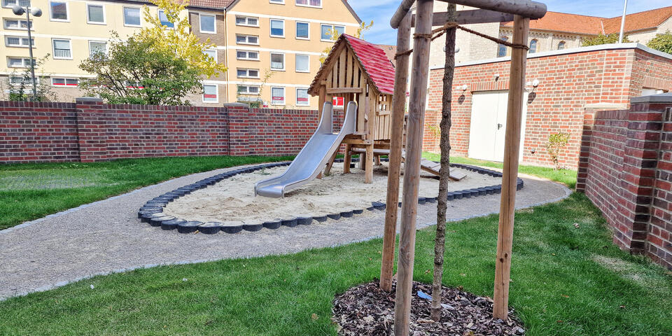 Eine Rutsche auf einem Außengelände mit Rasen. Im Hintergrund eine Kirche.