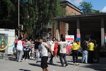 Menschen stehen plaudernd vor der Bühne und der Unterkunft.