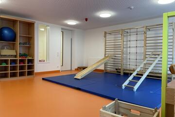 Ein Raum mit Turnmatten, Kletterwänden, Gymnastikbällen und Hockern.