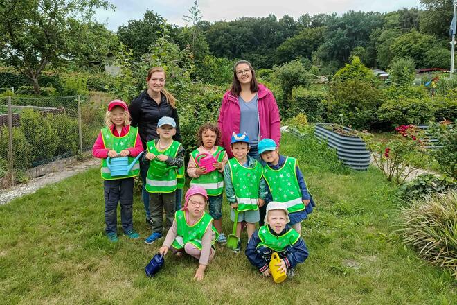 Schrebergarten der Johanniter-Kita Seehüpfer Eine Gruppe von Kindern und zwei Erzieherin stehen in einer Schrebergartenparzelle.