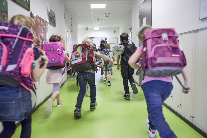 Gruppe Kinder eilt fröhlich durch den Schulflur nach draußen Richtung Hort.
