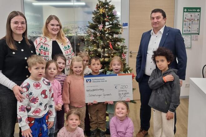 Einrichtungsleitung und Kinder des Kinderhauses, sowie der Filialleiter der Raiffeisenbank mit dem Spendencheck