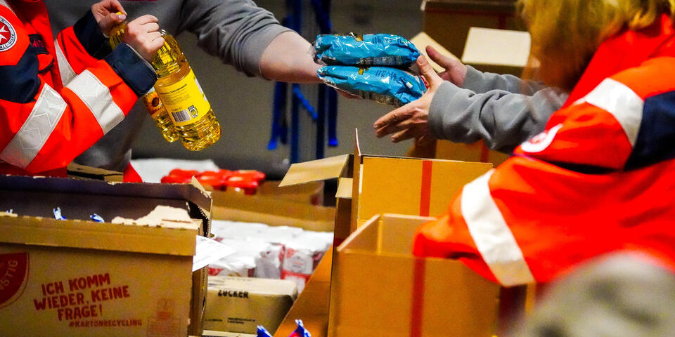 Frauen und Männer in Johanniter-Kleidung packen Lebensmittel in Pakete