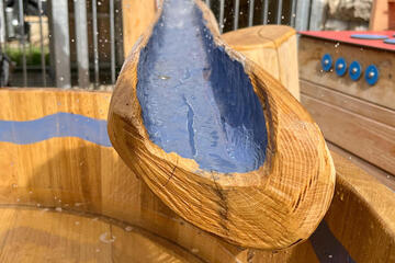 Teilausschnitt von einer Holzrinne durch die Wasser fließt