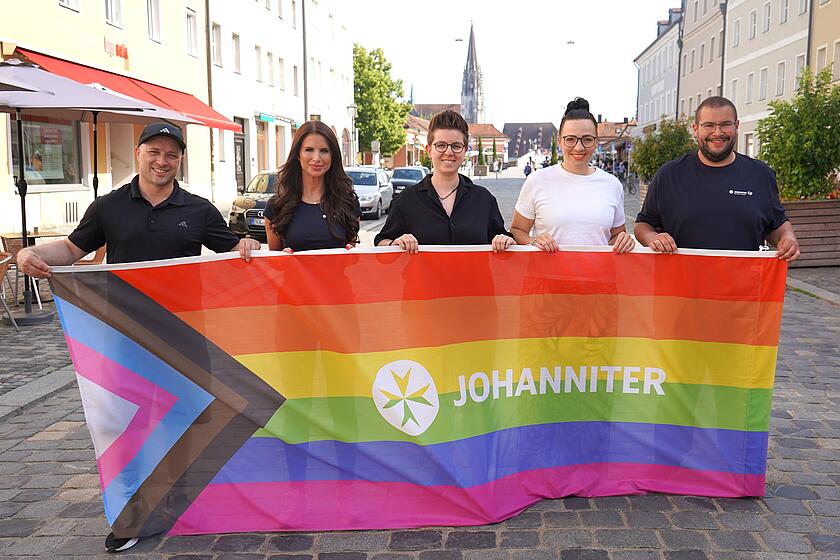 Anwesende halten Vielfalt-Flagge der Johanniter hoch