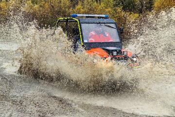 Ein Johanniter-Geländefahrzeug mit Blaulicht pflügt durch eine große Wasserpfütze, sodass eine hohe Gischt entsteht.