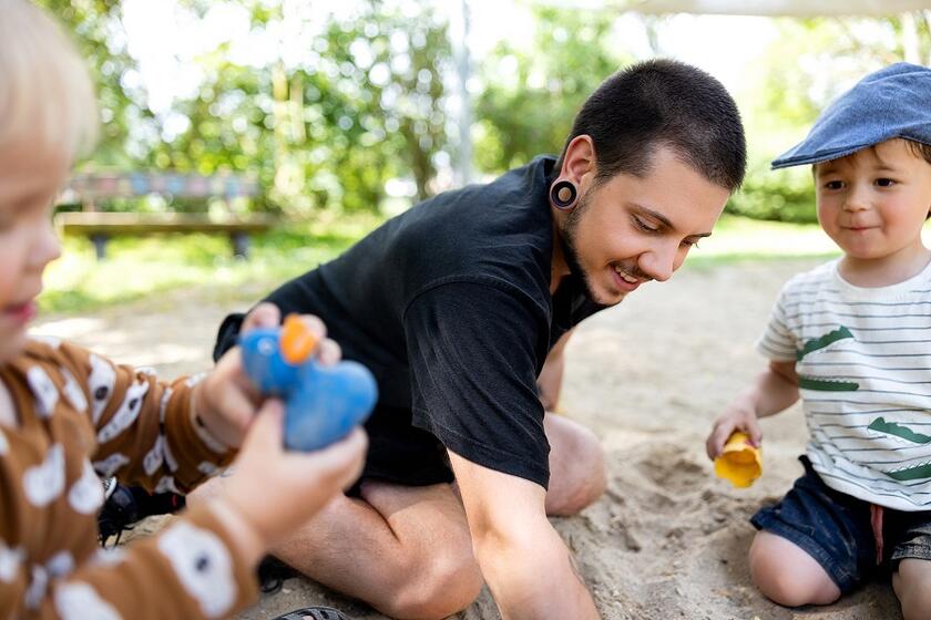 Ein Erzieher spielt mit Kindern im Sandkisten in der Kita
