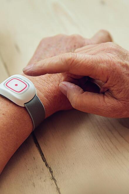 Eine Hand mit einem Hausnotrufknopf am Gelenk.