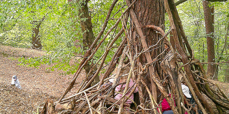 Kinder in einem selbstgebauten Tipi aus Ästen in einem Wald.