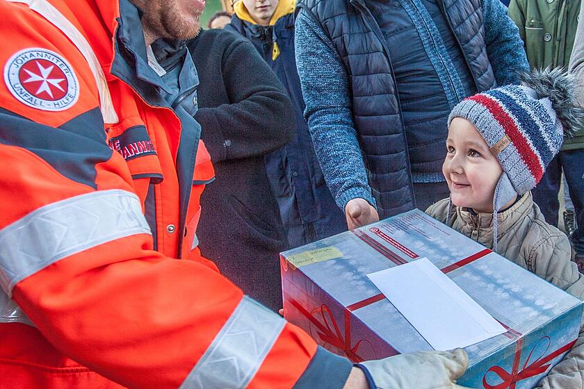 Mann übergibt Johanniter-Weihnachtstrucker Paket an Kind