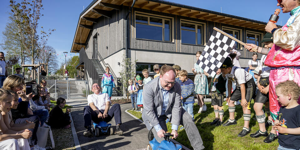 Kinder jubeln den Bürgermeistern zu, die auf Bobbycars um die Wette fahren.
