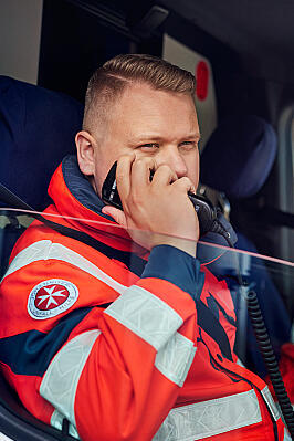 Ein Johanniter sitzt im Rettungswagen, das Fenster ist offen und er setzt einen Funkspruch ab