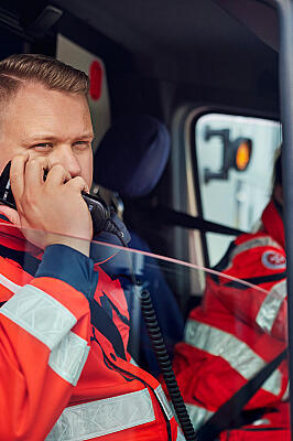 Johanniter in Einsatzkleidung im Rettungswagen, schaut aus dem Fenster und setzt einen Funkspruch ab