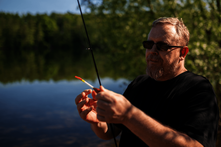 Ein Mann mit Sonnenbrille bereitet an einem ruhigen See eine Angelrute vor