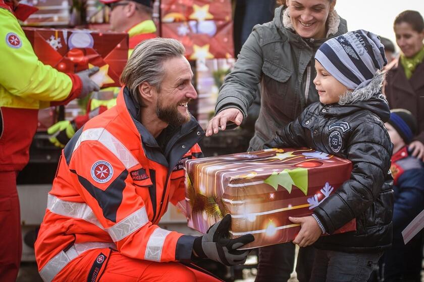 Ein Mitarbeiter der Johanniter überreicht einem kleinen Jungen ein Paket
