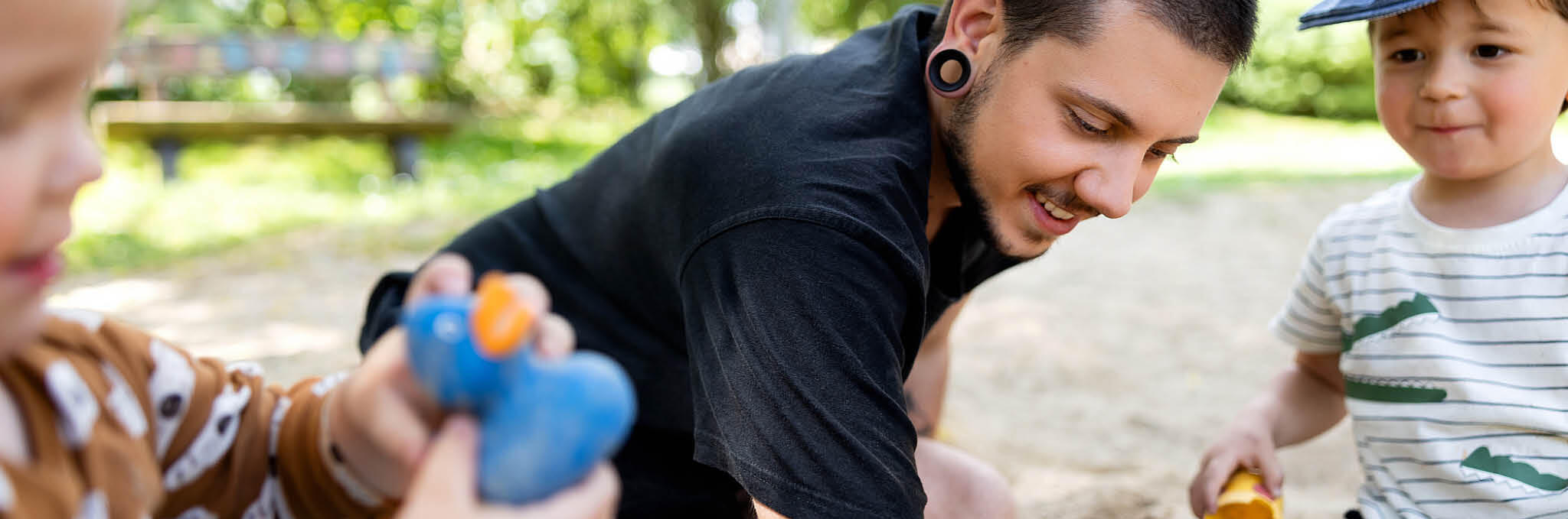 Ein Erzieher spielt mit Kindern im Sandkasten.