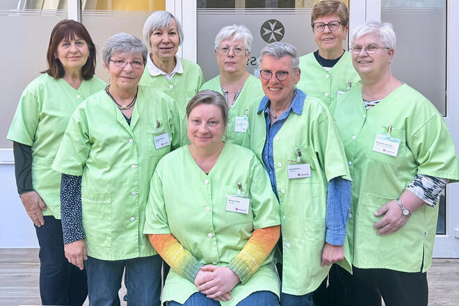 Gruppenbild von 8 älren Damen im typischen lindgrünen Kittel des Besuchsdienstes
