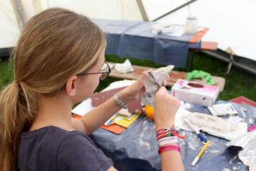Ein Mädchen sitzt in einem großen Zelt an einem Tisch und bastelt etwas.