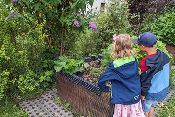 Zwei Kinder stehen an einem Hochbeet.