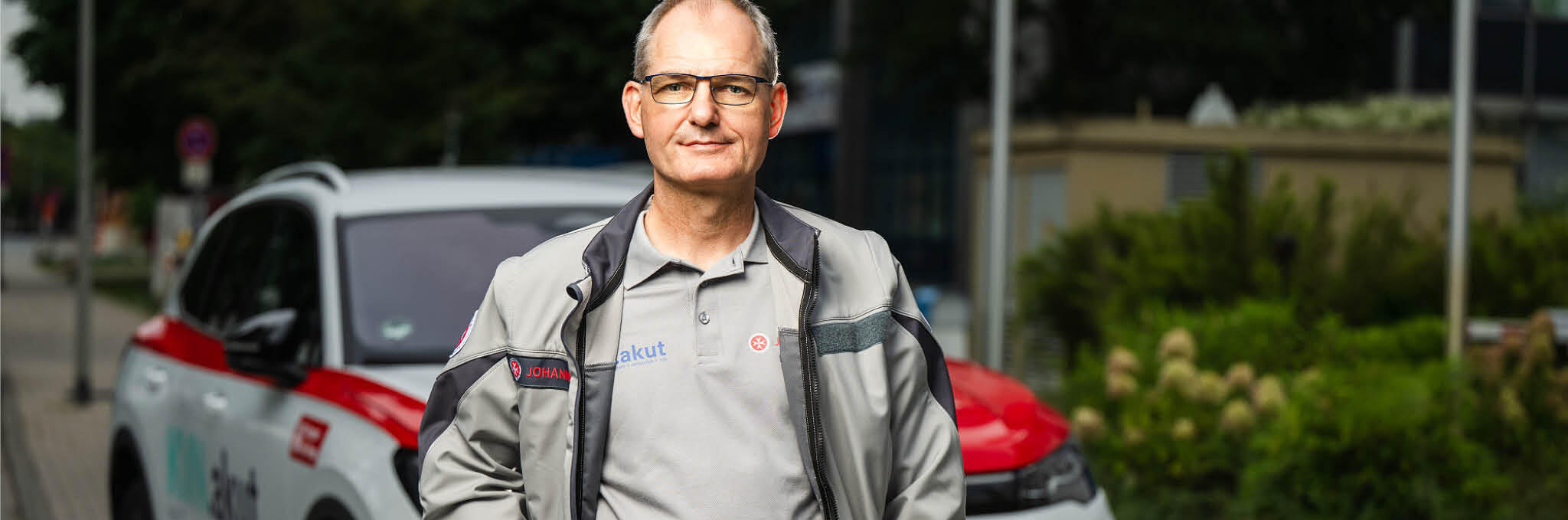 Ein Arzt im ärztlichen Bereitschaftsdienst steht vor einem Fahrzeug und schaut in die Kamera.