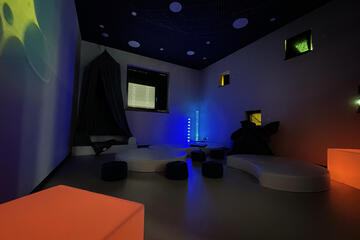 Ein abgedunkelter Raum mit Liegemöglichkeiten und gemütlichen bunten Lampen.