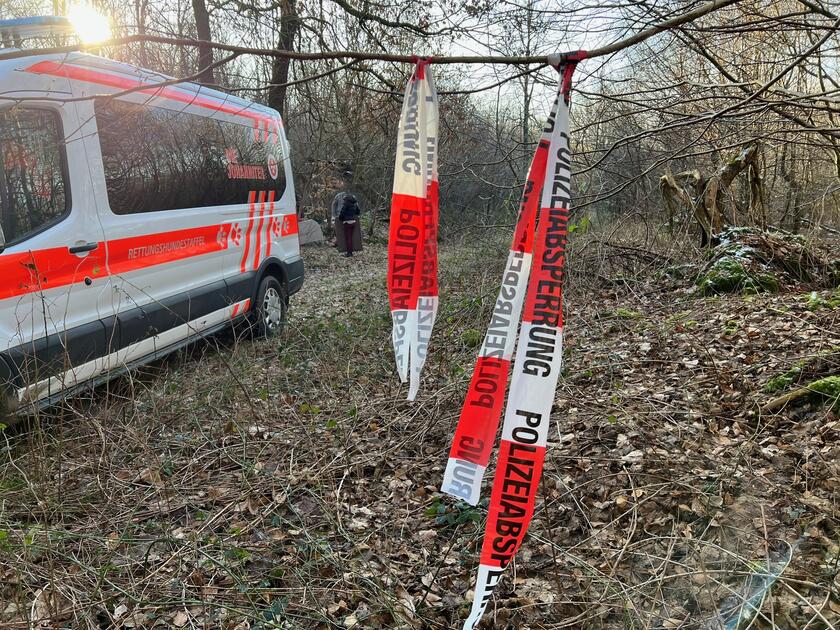In einem Waldstück steht ein Johanniter-Transporter, daneben ist ein Absperrband zu sehen.