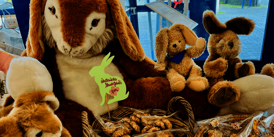 Große Plüschhasen auf Tisch, Körbe mit einzeln verpacktem Mandelgebäck davor.