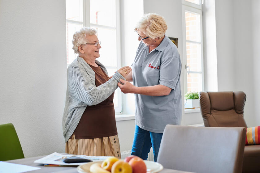 Eine häusliche Hilfe unterstützt eine ältere Dame beim Anziehen.