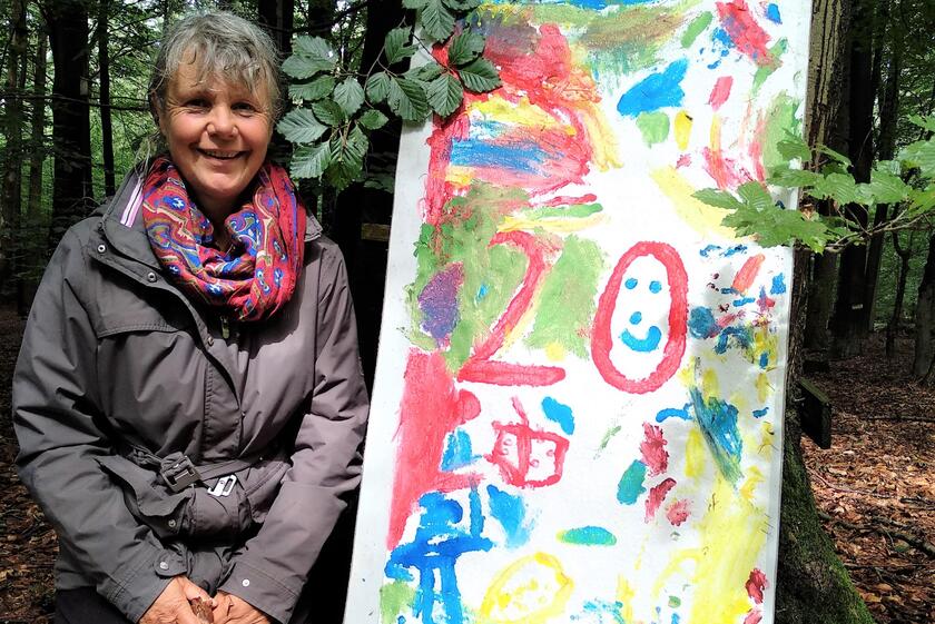Kita-Leitung Gudrun Stötzer kniet neben dem Bild, das die Kinder zum Jubiläum gemalt haben.