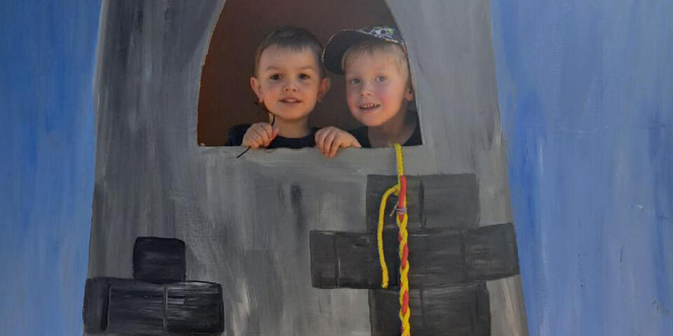 Zwei Kinder schauen aus einem Turm, der aus Pappe errichtet wurde, ähnlich dem Märchen Rapunzel.