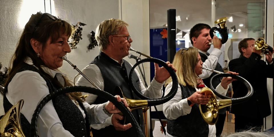 eine Gruppe Jagdhornbläser in weißen Hemden und grauen Westen spielt auf unterschiedlich großen Hörnern