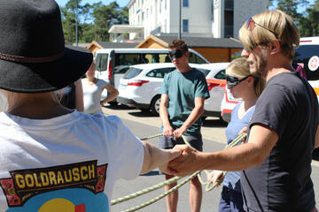 Junge Erwachsene stehen im Kreis, haben die Augen verbunden und halten sich an den Händen