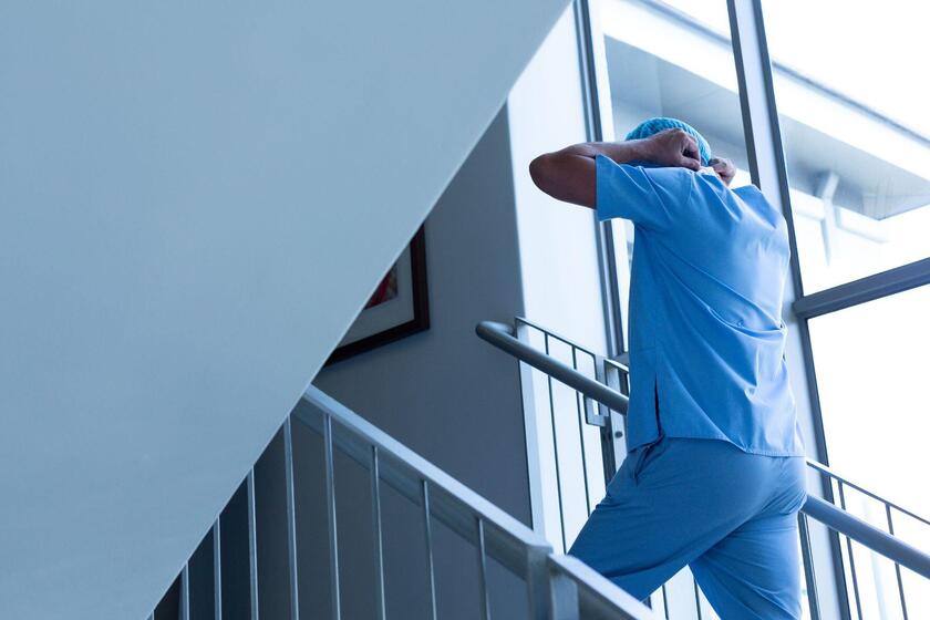 Maennliche Pflegekraft in blauer Arbeitskleidung steigt Treppe hinauf