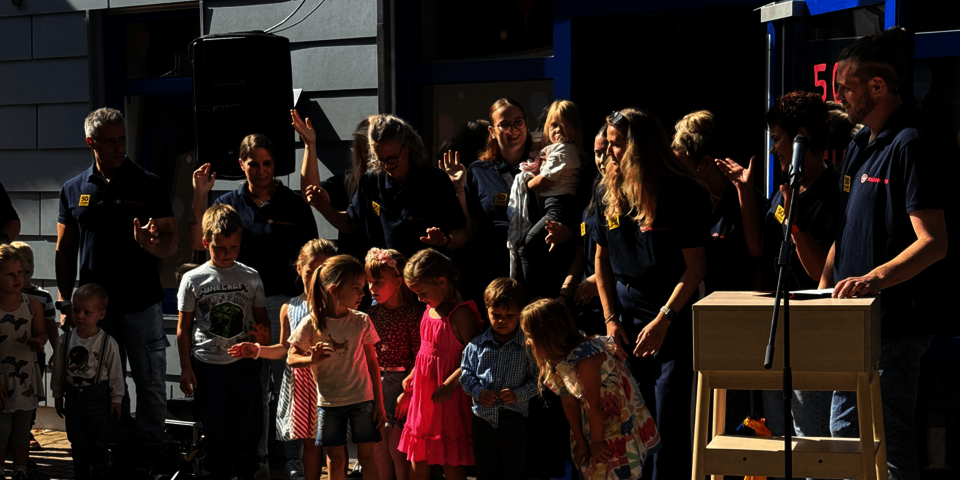 Erwachsene im Teamshirt und Kinder stehen aufgereiht zusammen bei einer Feier im Freien.