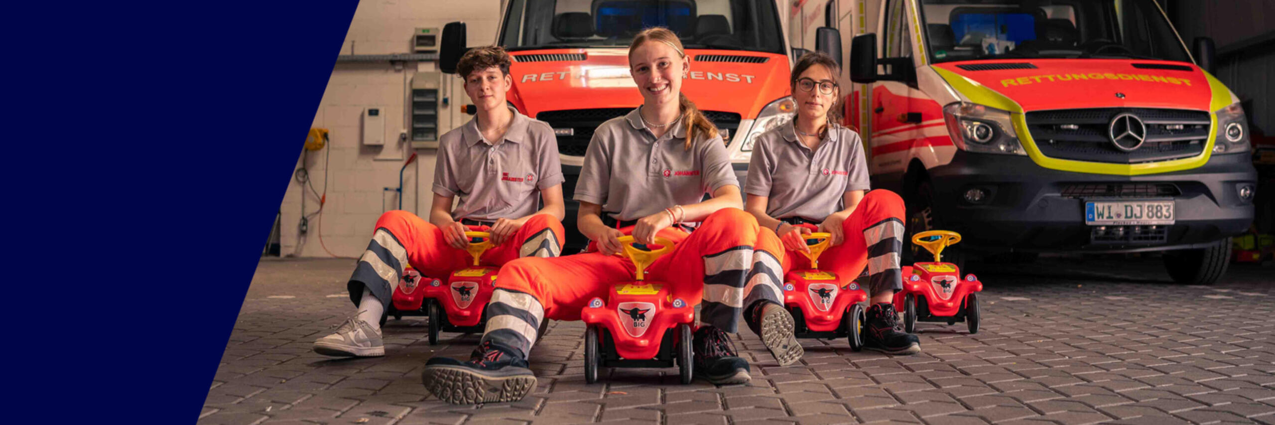 Mehrere FSJlerinnen der Johanniter in Wiesbaden sitzen auf Bobbycars vor einem Rettungswagen.