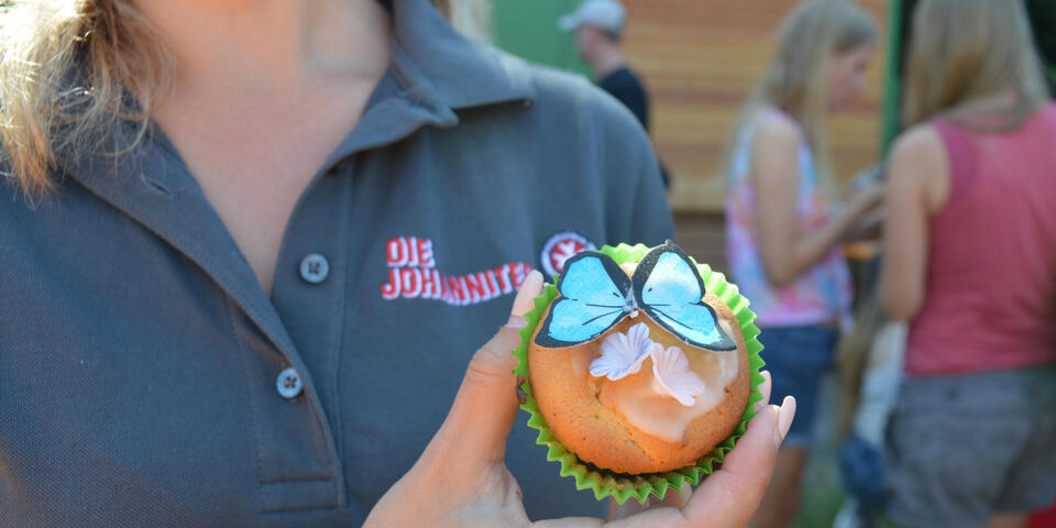 Ein bunt verzierter Cupcake wird in die Kamera gehalten
