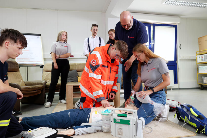 Eine Gruppe junger Menschen kniend an einer Übungspuppe. Ein Mann in Johanniter-Kleidung beugt sich zu ihnen. Andere schauen zu.