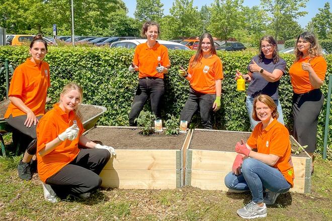 Mehrere Sixt Mitarbeiter halten einen Daumen hoch und stehen neben einem Blumenbeet.