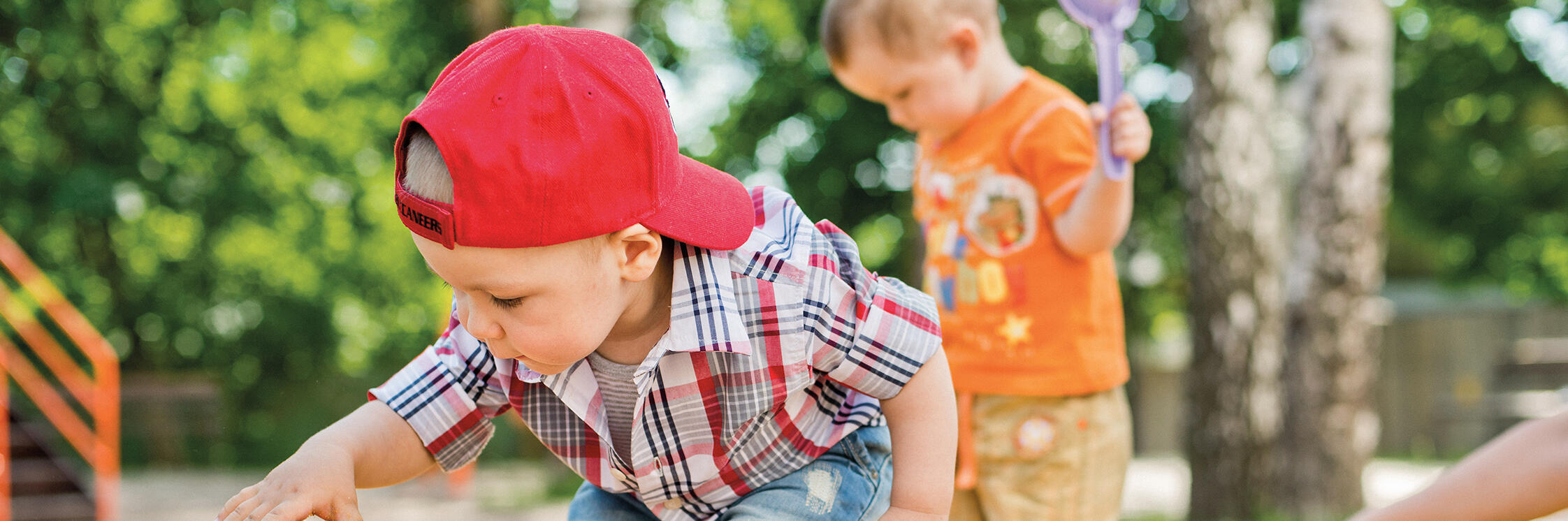 Kleiner Junge mit roter Mütze spielt im Sandkasten mit einem Auto