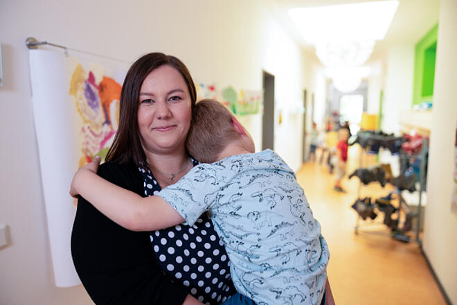 Eine Erzieherin in einer Johanniter-Kita trägt ein Kind auf dem Arm. Sie lächelt freundlich in die Kamera.