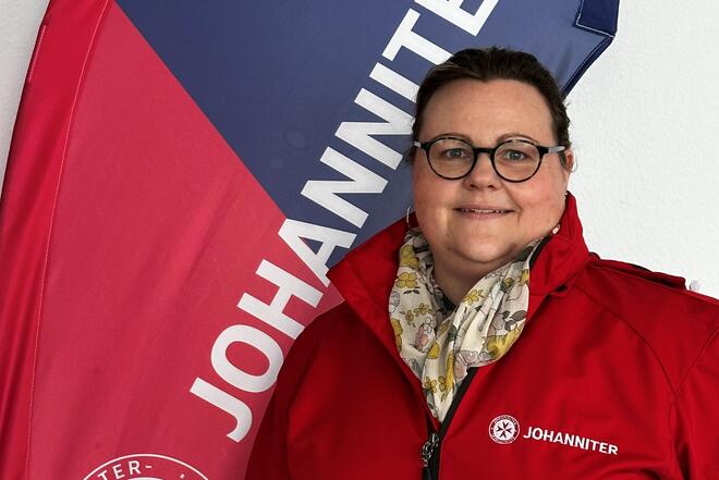 Mitarbeiterin in Dienstkleidung vor Johanniter-Flagge