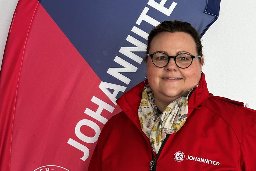 Mitarbeiterin in Dienstkleidung vor Johanniter-Flagge