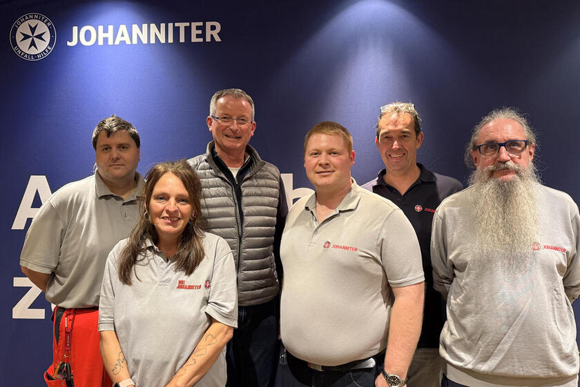 Eine Gruppe von Menschen schaut in die Kamera, darunter fünf Johanniter und ein Herr im Anzug.