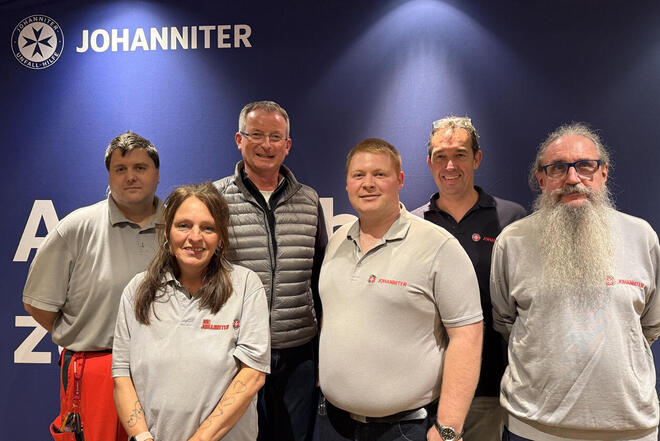 Eine Gruppe von Menschen schaut in die Kamera, darunter fünf Johanniter und ein Herr im Anzug.