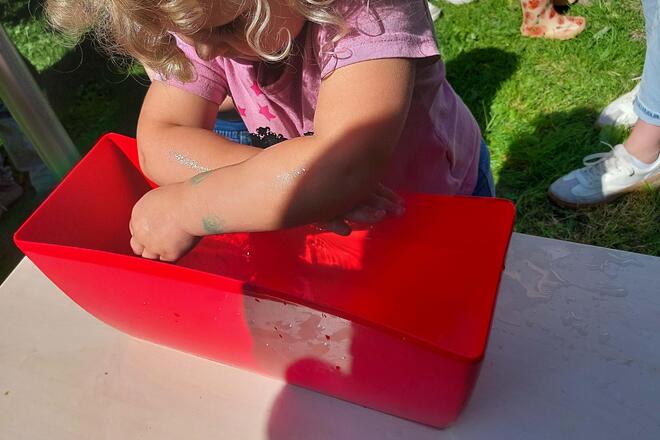 Ein Kind taucht seine Unterarme in eine Wanne mit Wasser.