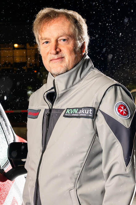 Ein Arzt im ärztlichen Beritschaftsdienst bei den Johannitern steht neben einem Fahrzeug.